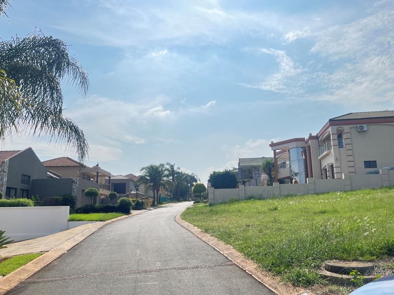 A view of a paved residential street within a well-maintained estate, featuring surrounding homes and landscaped green spaces.