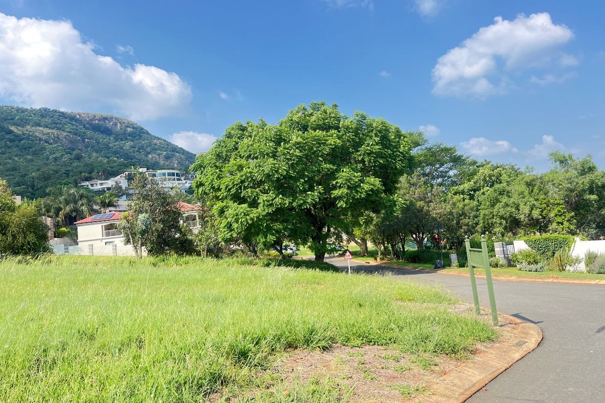 A view of a vacant residential plot featuring established trees, grassy terrain, and paved road access in a scenic neighborhood setting.