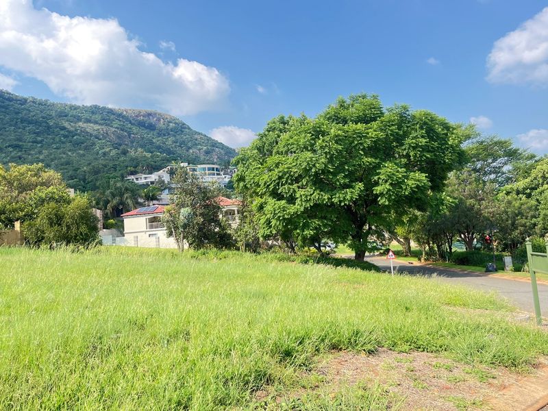A vacant residential plot featuring established trees and surrounding mountain views, situated in a quiet neighborhood setting.