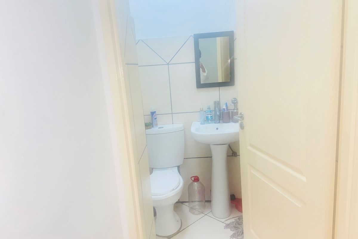 A compact bathroom featuring a pedestal basin, toilet, and neutral ceramic wall and floor tiling.