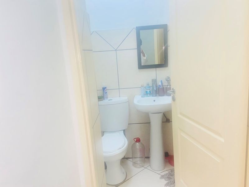 A compact bathroom featuring a pedestal basin, toilet, and neutral ceramic wall and floor tiling.