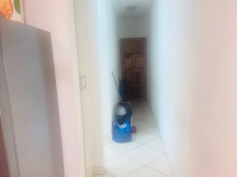 A simple interior hallway featuring tiled flooring and a wooden door, providing access between rooms in the apartment.