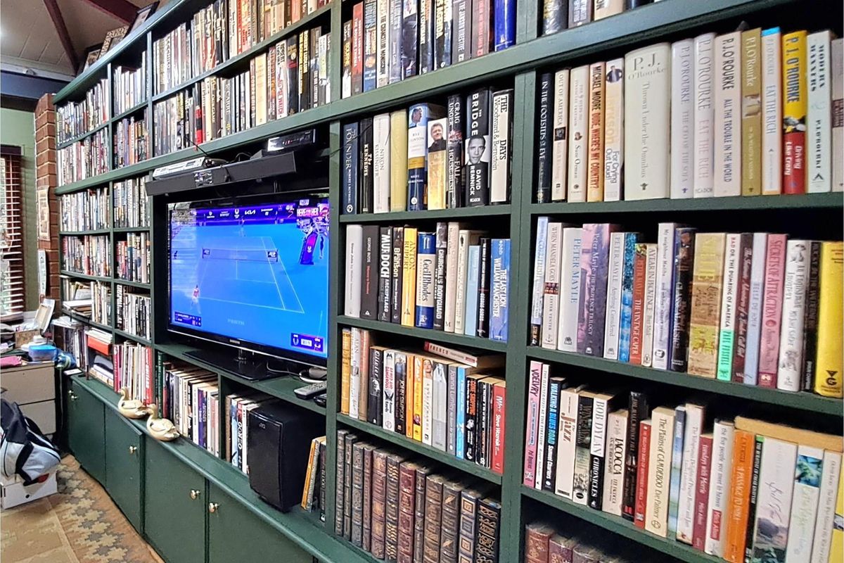 A large, floor-to-ceiling built-in dark green wooden bookshelf unit featuring integrated shelving and a central recessed space for a television.