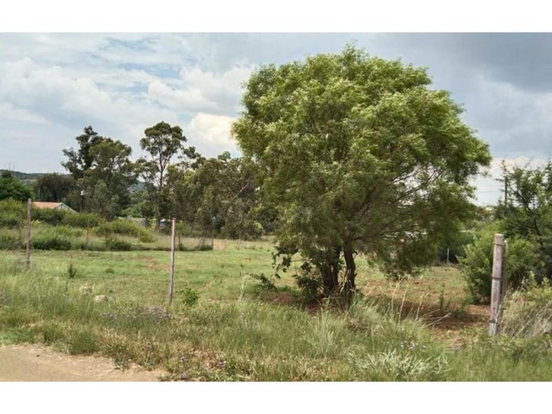 A view of a vacant residential plot featuring natural grassland, mature trees, and existing wire perimeter fencing.