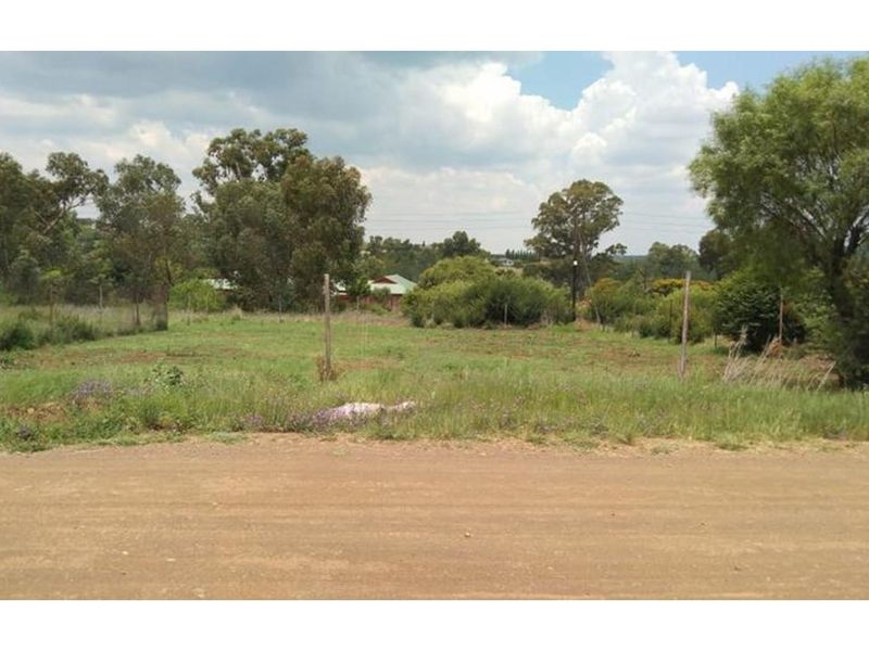 A vacant residential plot featuring natural vegetation, wire fencing, and direct access from an unpaved road.