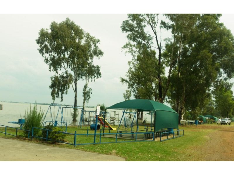 Outdoor recreational area featuring a playground with shade sail, perimeter fencing, and direct access to the waterfront.