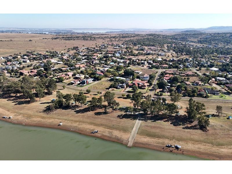 Aerial view of a residential area situated along a waterfront, featuring a concrete boat ramp and surrounding natural landscape.