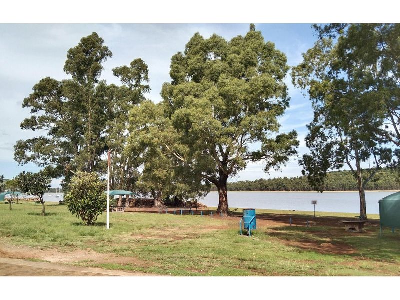 A scenic waterfront garden area featuring mature trees, open grassed space, and direct access to the lake.