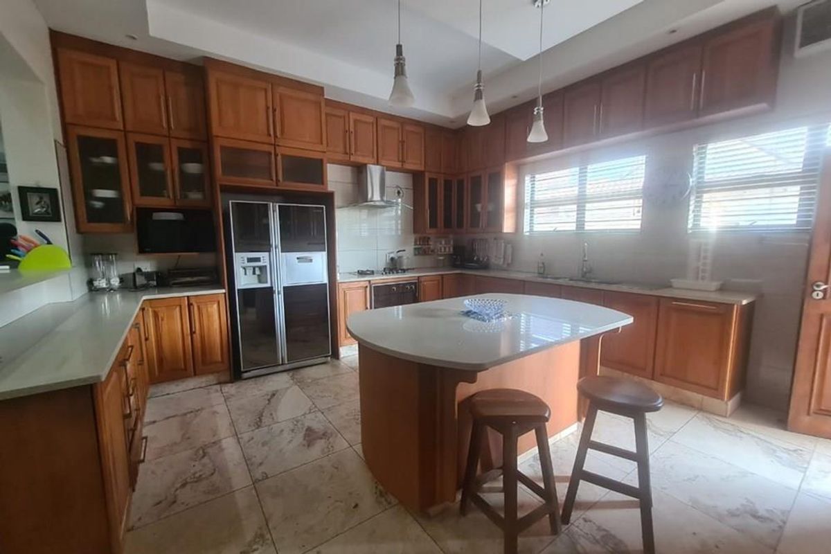 Spacious kitchen featuring extensive wooden cabinetry, a central island with stone countertop, built-in oven, extractor fan, and tiled flooring.