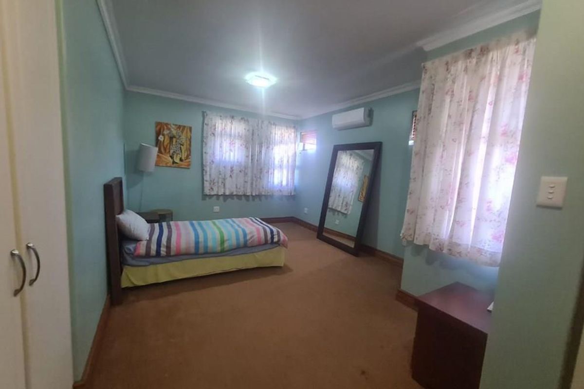 A bedroom featuring light blue walls, carpeted flooring, a wall-mounted air conditioning unit, and built-in wardrobe storage.