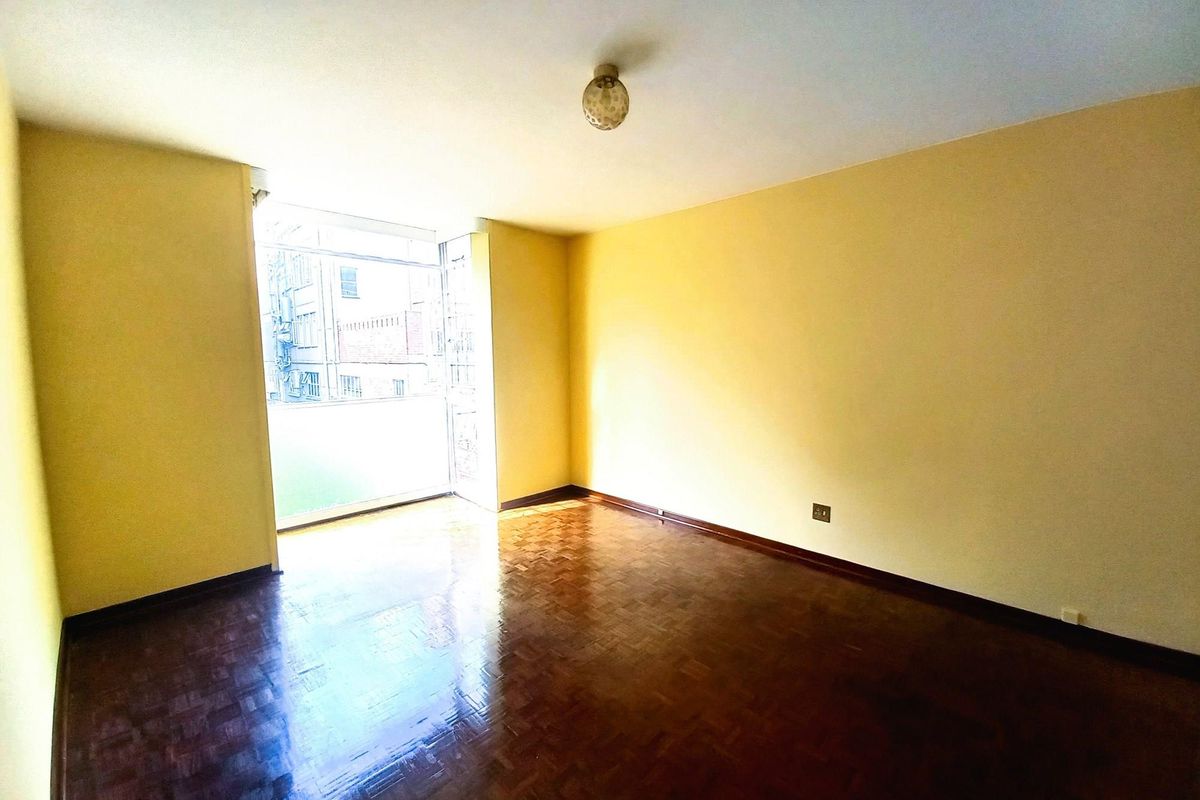 A vacant room featuring polished parquet flooring, yellow-toned walls, and a large window providing natural light and access to a small balcony area.