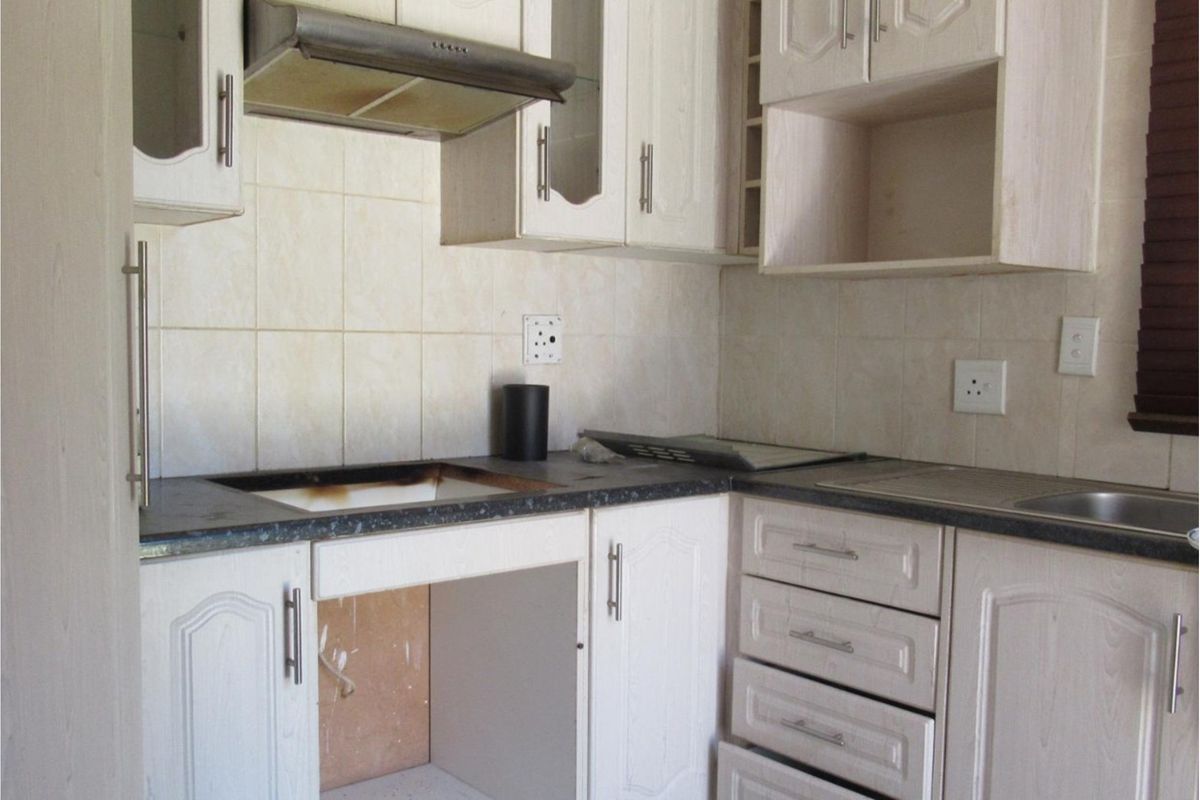 A dated kitchen featuring white cabinetry, a tiled backsplash, and a dark countertop, currently missing built-in cooking appliances.