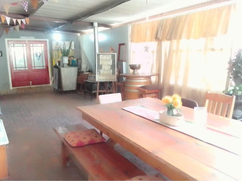 A covered patio area featuring brick flooring, a corrugated metal roof, and double door access, suitable for casual dining or social gatherings.