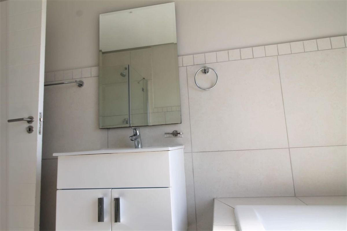 A clean, modern bathroom featuring a white vanity cabinet, wall-mounted mirror, and tiled wall finishes with chrome fixtures.