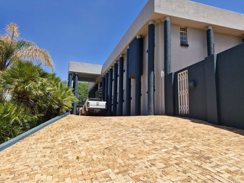 Front exterior view of the property featuring a paved driveway, modern architectural columns, and secure perimeter walling.