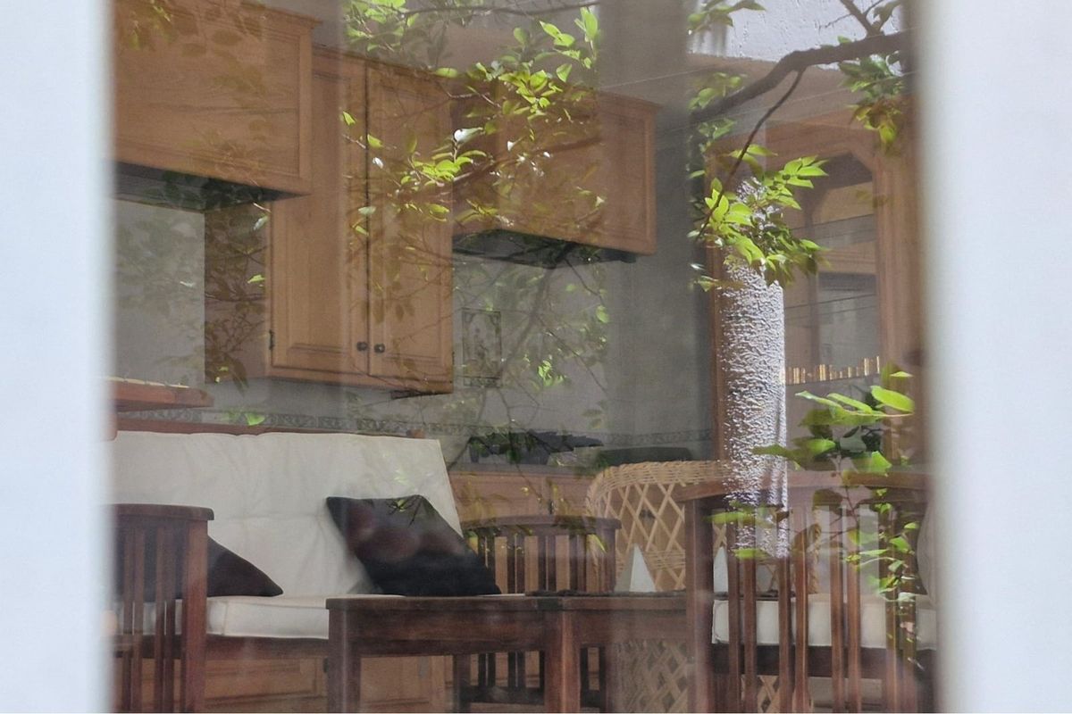 A view through a window showing a kitchen area with wooden cabinetry and a tiled backsplash.