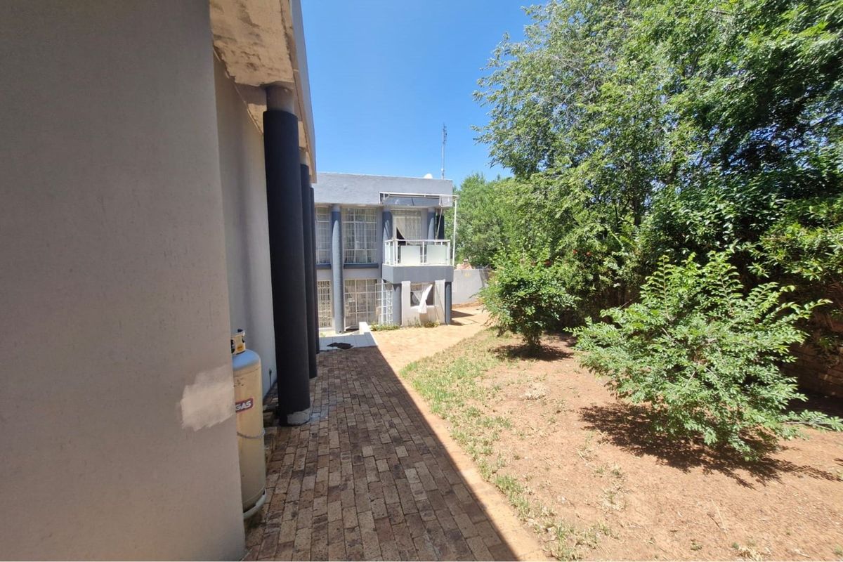A view of the rear exterior of the house featuring a paved walkway, garden area, and a multi-level structure with a balcony.