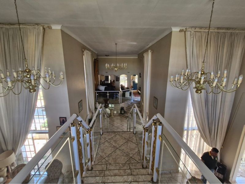 Grand entrance hallway featuring a central staircase with decorative railings, tiled flooring, and dual classic chandeliers overlooking the lower living area.