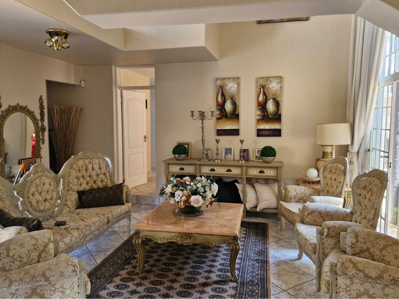 A spacious living room featuring tiled flooring, high ceilings, and large windows that provide ample natural light.