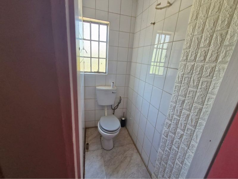 A compact bathroom featuring white wall tiling, a standard toilet, and a small window, requiring cosmetic updates to modernize the space.