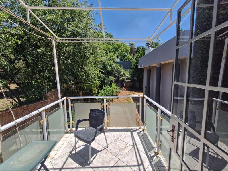 A private balcony featuring a metal pergola frame, glass and metal balustrades, and tiled flooring, overlooking a lush garden area.