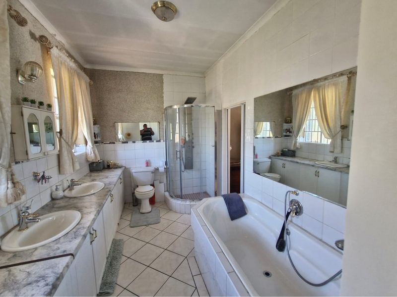 A spacious bathroom featuring a double vanity with marble-look countertop, a corner shower unit, a built-in bathtub, and tiled flooring.
