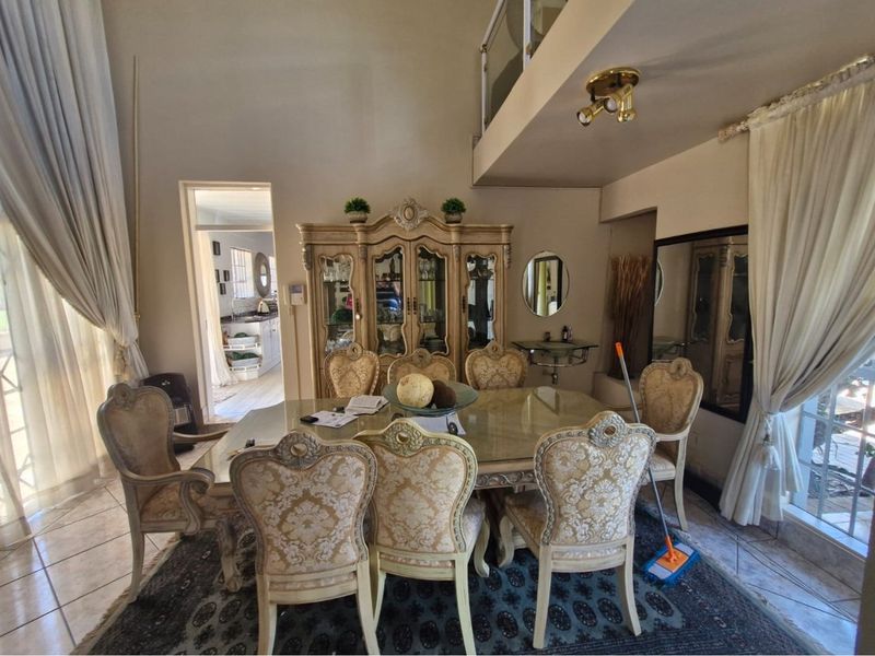 A formal dining area featuring high ceilings, tiled flooring, and a mezzanine level overlooking the space, with direct access to the kitchen.