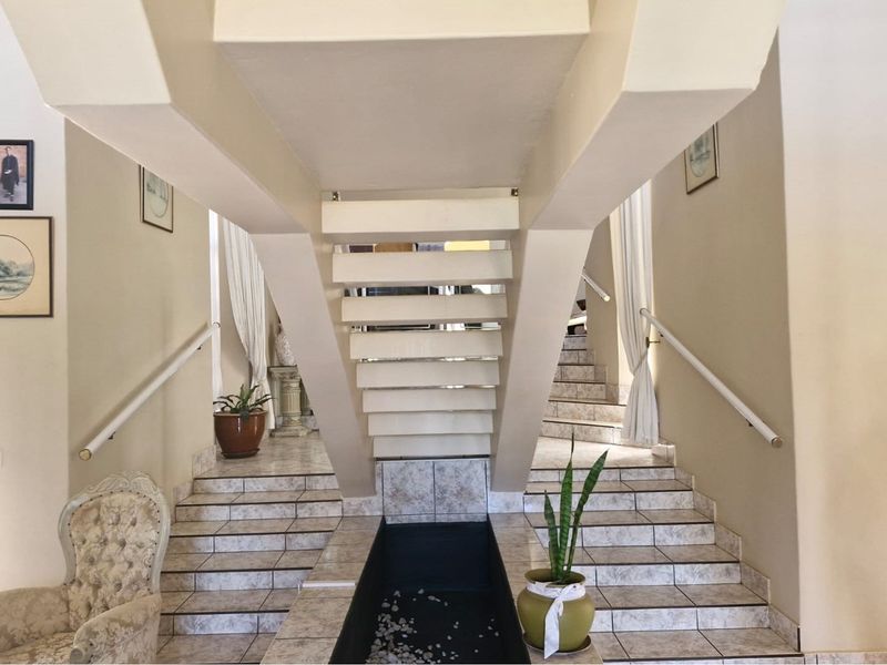 A grand entrance hall featuring a split staircase design with tiled steps and a central decorative water feature or planter base.
