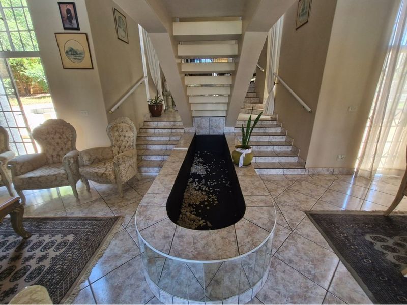 Spacious entrance hall featuring a central decorative water feature and a split staircase with tiled flooring and large windows providing natural light.