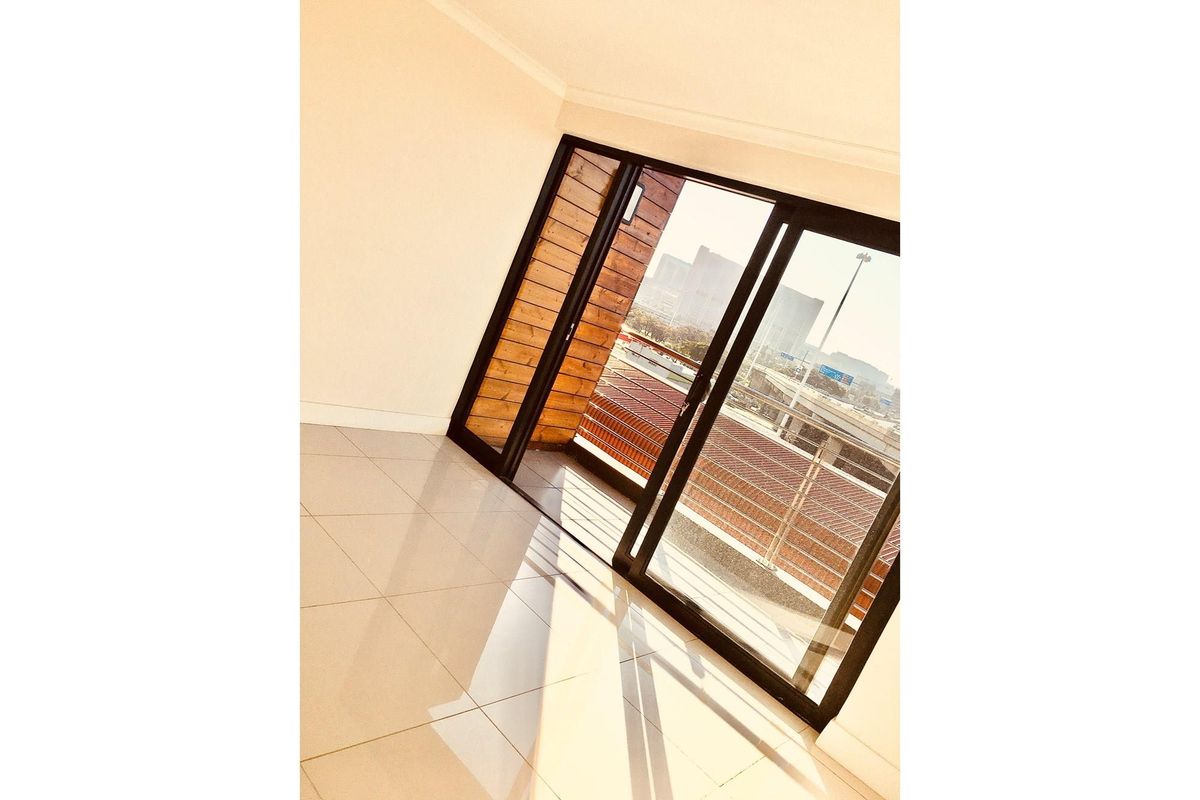 Bright living area featuring large sliding glass doors that open onto a private balcony with urban views and tiled flooring throughout.