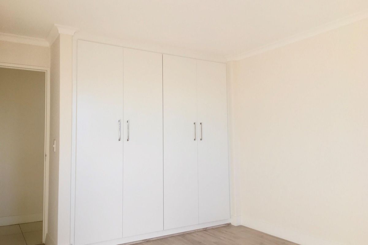 A bright bedroom featuring built-in floor-to-ceiling wardrobes with modern handles and light-toned wood-look flooring.
