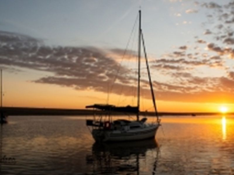 A scenic sunset view over the water featuring sailboats, highlighting the tranquil landscape and natural surroundings of the area.