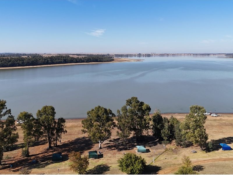 An aerial view of the vacant residential land featuring direct lake frontage and established trees, offering scenic water views.