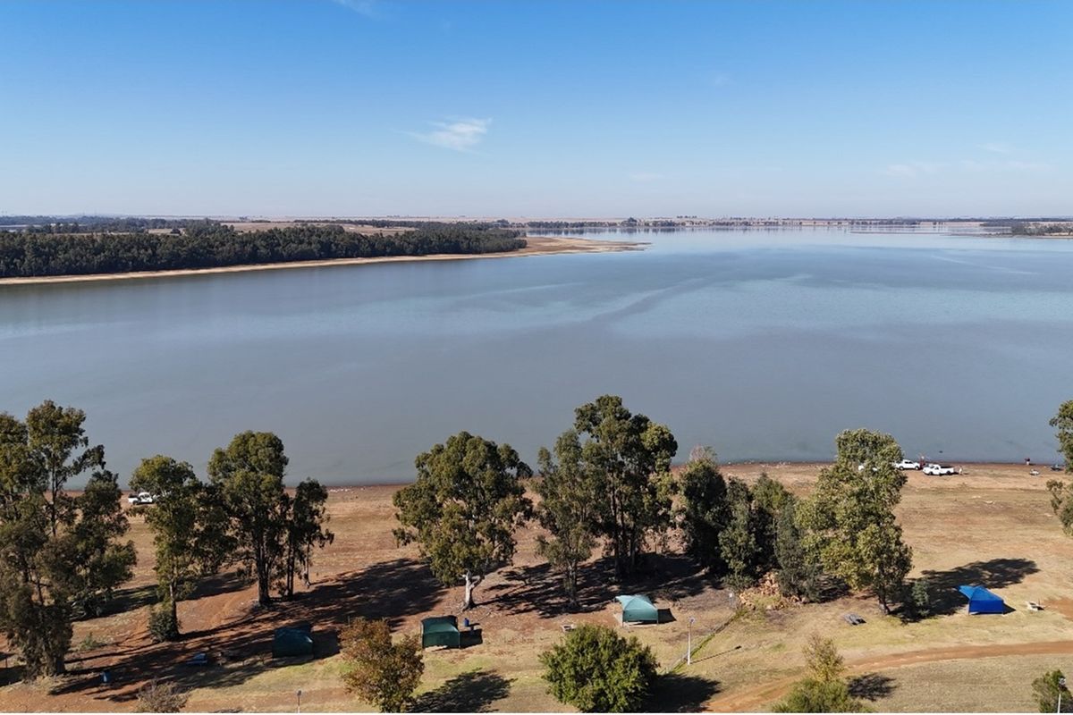 An aerial view of the vacant residential land featuring direct lake frontage and established trees, offering scenic water views.