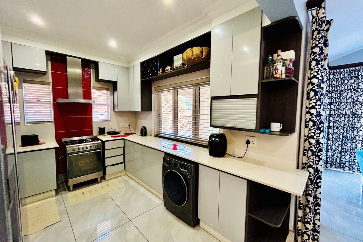 Modern kitchen featuring high-gloss cabinetry, stone countertops, a stainless steel gas stove with extractor fan, and integrated laundry appliance space.