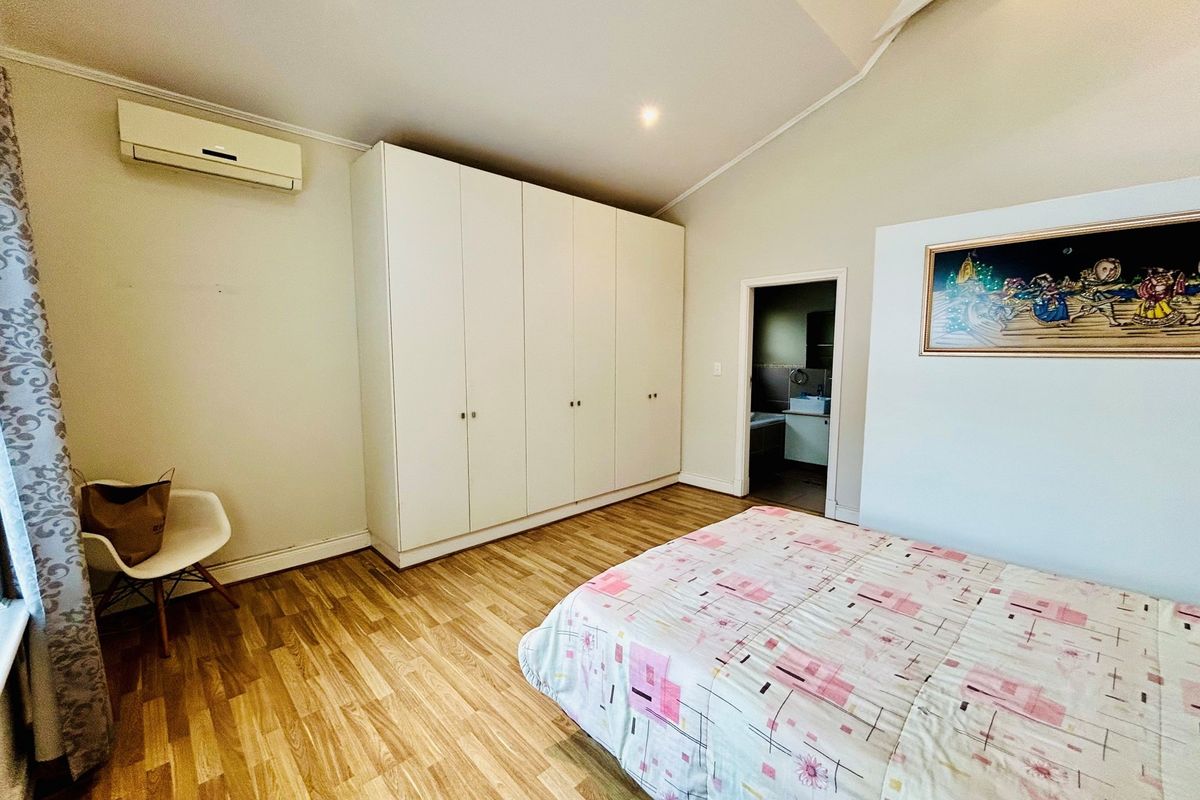 Spacious bedroom featuring light wood-look flooring, built-in floor-to-ceiling wardrobes, a wall-mounted air conditioning unit, and an en-suite bathroom access.