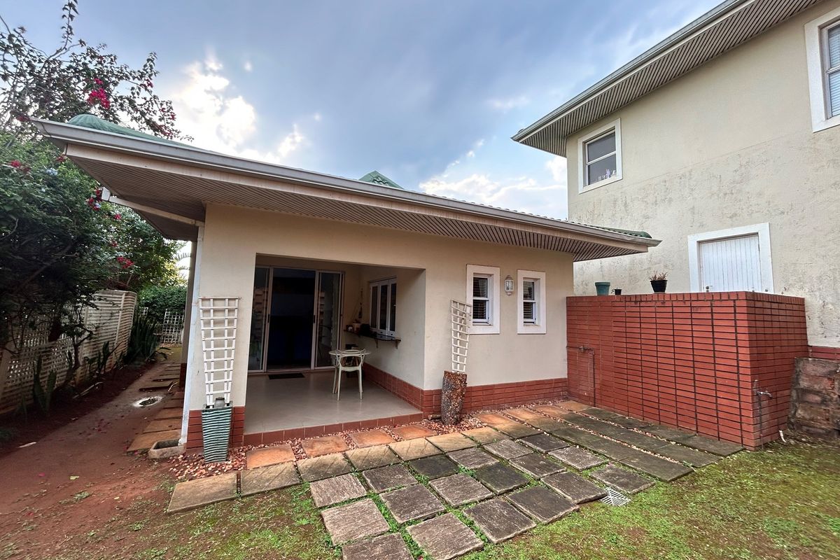 A rear view of the townhouse featuring a covered patio area, paved courtyard, and established garden space.