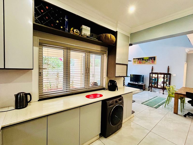 Modern open-plan kitchen featuring sleek cabinetry, stone countertops, and integrated laundry appliance, flowing seamlessly into the adjacent dining and living area.