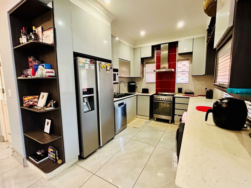 Modern kitchen featuring high-gloss cabinetry, stone countertops, a stainless steel gas stove with extractor fan, and tiled flooring.
