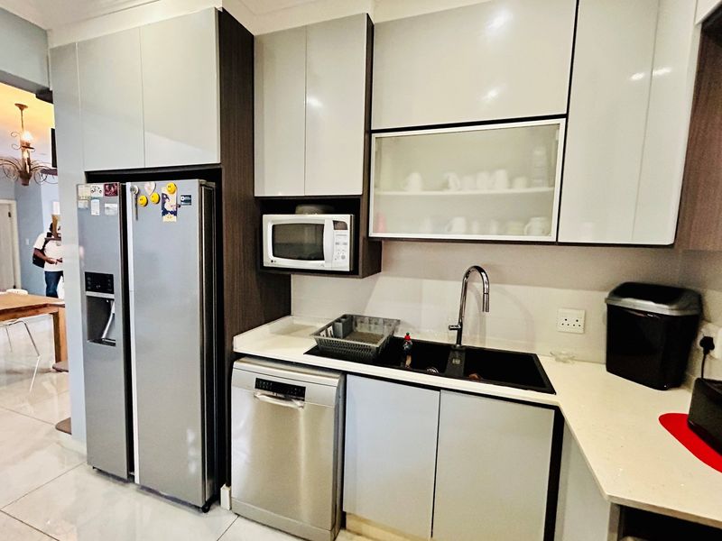 Modern kitchen featuring high-gloss cabinetry, stone countertops, a double-basin sink with a gooseneck faucet, and integrated appliance housing.