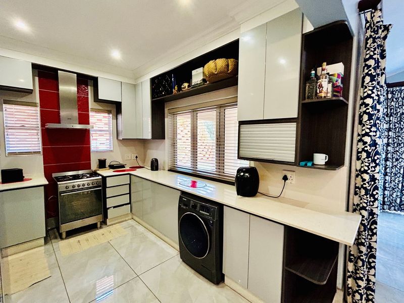 Modern kitchen featuring high-gloss cabinetry, stone countertops, a stainless steel gas stove with extractor fan, and integrated laundry appliance space.