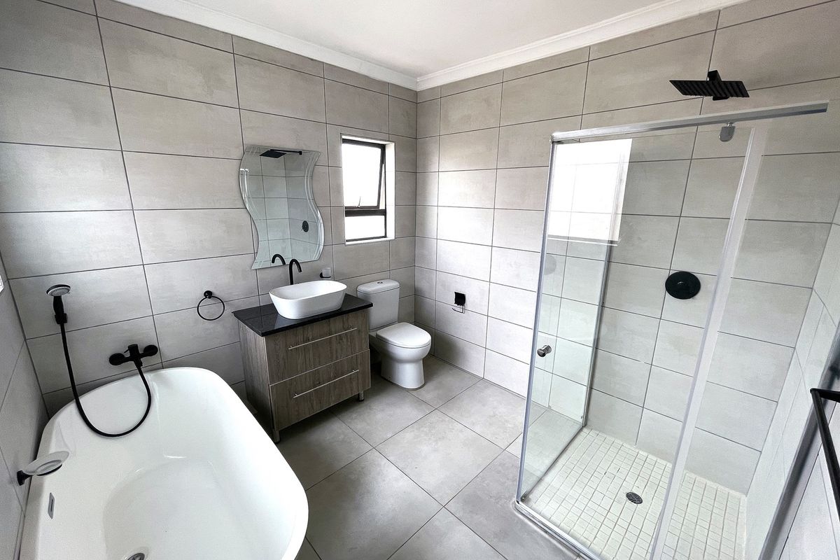 Modern bathroom featuring a freestanding bathtub, glass-enclosed shower, vanity with vessel sink, and contemporary grey wall and floor tiling.