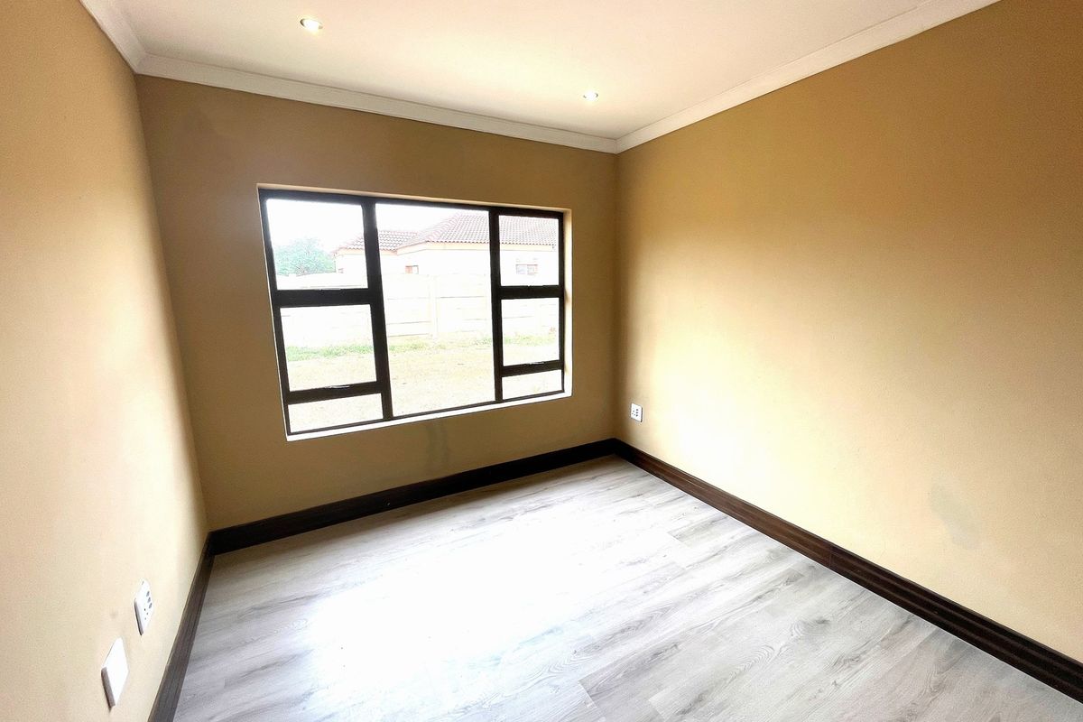 A bright, empty bedroom featuring modern light-toned laminate flooring, dark skirting boards, and recessed ceiling downlights.