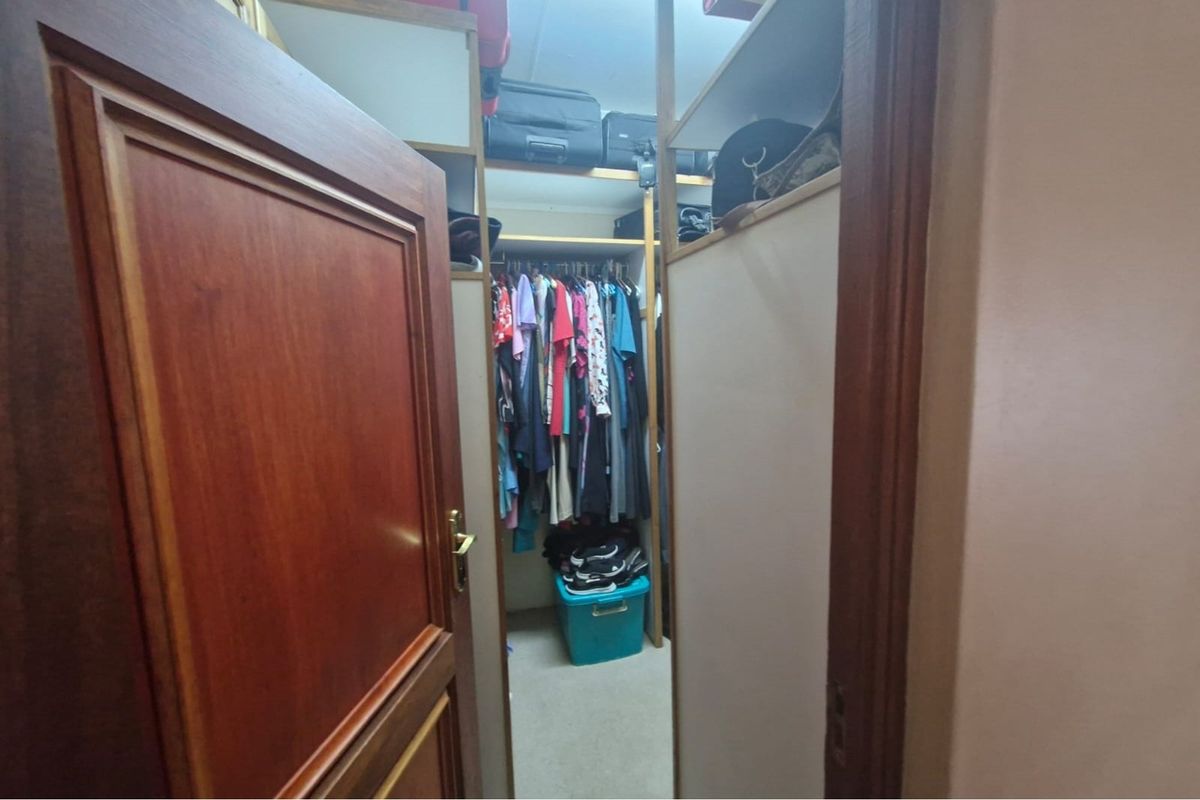 A walk-in closet or dressing area featuring built-in shelving and hanging rails, accessed via a solid timber door.