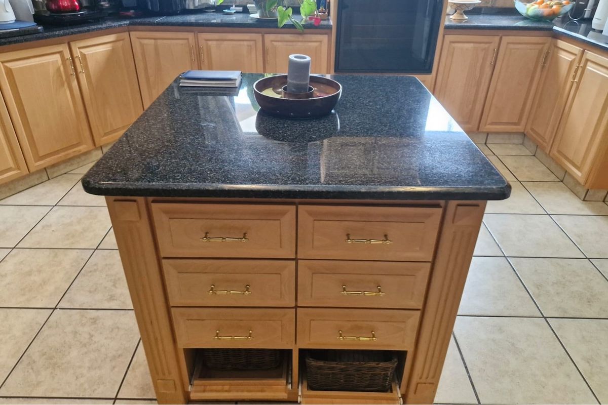 A functional kitchen featuring a central island with granite countertops, light wood cabinetry, and ceramic floor tiles.