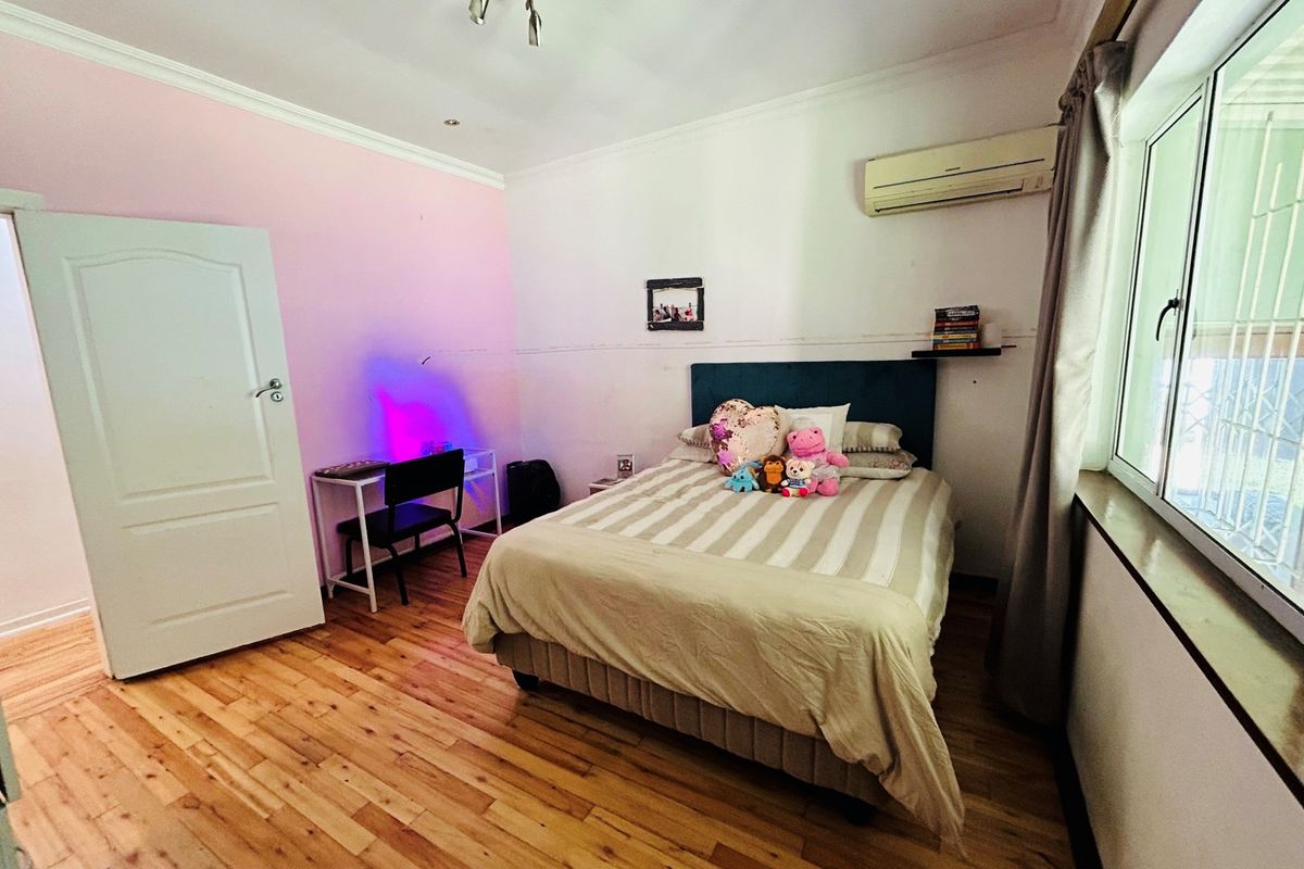 A bedroom featuring light wood flooring, a wall-mounted air conditioning unit, and a window with security bars.