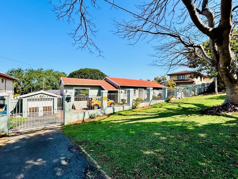 Front exterior view of the property featuring a tiled roof, perimeter wall with metal fencing, gated driveway, and a well-maintained lawn.