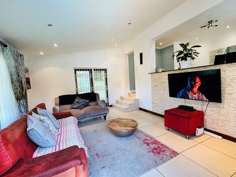 A spacious living room featuring tiled flooring, recessed downlighting, and a decorative stone-cladded feature wall with integrated television mounting.