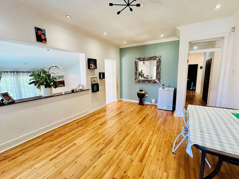 Spacious open-plan living and dining area featuring polished hardwood flooring, recessed downlighting, and a large pass-through window connecting to the adjacent room.