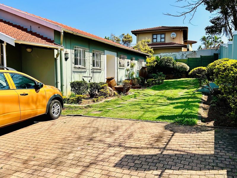 A side view of the property featuring a paved driveway, a well-maintained lawn, and established garden beds alongside the building exterior.